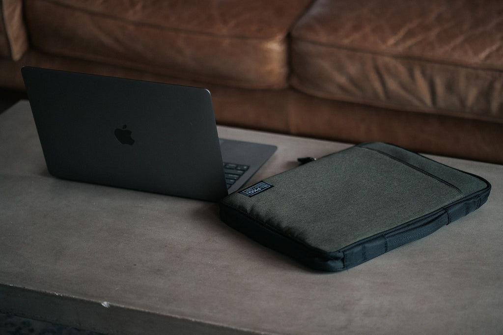 PKG Stuff Recycled Laptop Sleeve (evergreen) resting on table beside laptop